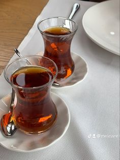 two cups of tea on a plate with spoons