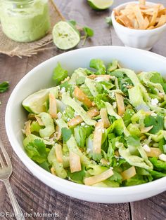 a white bowl filled with lettuce and other food items next to a fork