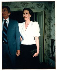 a man and woman standing next to each other in front of a wallpapered room