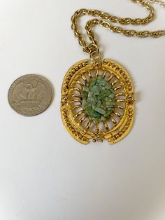 Pretty vintage gravel pendant necklace! Gold tone metal chain and pendant. Pendant has green gravel in the center. Pull back C style clasp. No makers mark. Overall good condition. Free of rust and verdigris. Minor wear to the gold tone in a few spots on the pendant. Pendant is 2 and 1/8 inches tall including the top loop and widest point is 1 and 1/2 inches. Chain end to end measures 20 and 1/4 inches. Discounts offered for bulk purchases. Shop accepts PayPal, credit cards, and Etsy gift cards. Retro Green Oval Jewelry, Vintage Gold Necklaces With Patina, Green Necklace With Large Medallion Pendant, Vintage Metal Necklace With Patina, Vintage Green Necklace With Chain, Vintage Green Brass Jewelry, Vintage Patina Metal Necklace, Green Metal Costume Jewelry Necklace, Vintage Green Metal Necklace