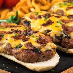 two hamburgers with cheese and bacon on them sitting on a plate next to some onion rings