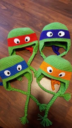 three crocheted hats with googly eyes are on top of a wooden table