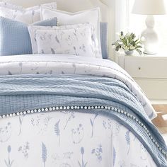 a bed with blue and white comforters, pillows and blankets on top of it