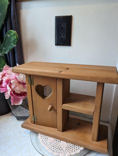 a wooden birdhouse with a hole in the side and a pink flower next to it