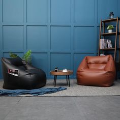 two leather chairs and a table in front of a blue wall