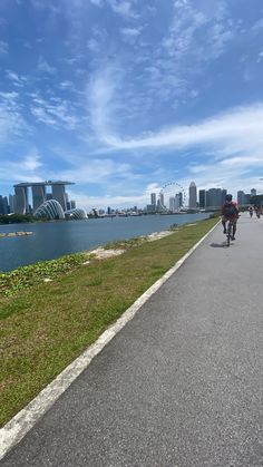 people riding bikes on the road near water and buildings in the background with blue sky