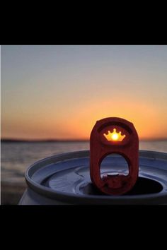 a beer can with a crown on it sitting in front of the ocean at sunset