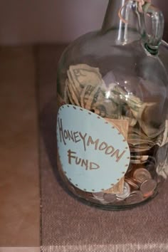 a glass jar filled with money sitting on top of a wooden table next to a sign that says honeymoon fund