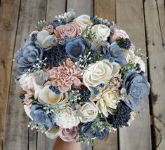 a bridal bouquet with blue and white flowers on a wooden table in front of wood planks