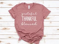 Celebrate the spirit of Thanksgiving with our "Grateful, Thankful, Blessed" T-Shirt. This shirt beautifully captures the essence of the holiday, reminding us to count our blessings and express gratitude. Printed on unisex Bella + Canvas 3001 pre-shrunk, airlume combed ring-spun cotton t-shirts that are super soft with a relaxed fit.  *Superior Quality *Retail Fit *Tear Away Labels *Unisex Sizing *Solid colors are 100% Cotton *Heather Colors are 52% Cotton/48% Poly *Athletic Heather is 90% Cotton Pink Soft-washed T-shirt For Fall, Inspirational Crew Neck T-shirt For Fall, Fall Gift T-shirt With Short Sleeves, Fall Season T-shirt Gift, Short Sleeve T-shirt For Fall Gift, Fall Pink Pre-shrunk T-shirt, Inspirational Graphic Print T-shirt For Fall, Inspirational Cotton T-shirt For Fall, Letter Print T-shirt As Fall Gift