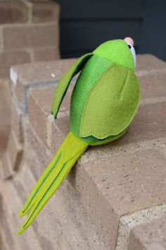 a green stuffed animal sitting on top of a brick wall