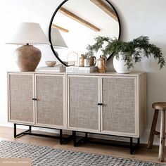 a sideboard with a mirror and vases on it in front of a lamp