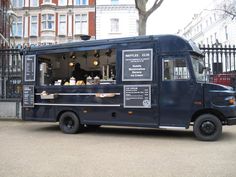 a blue food truck parked in front of a fenced area with buildings behind it