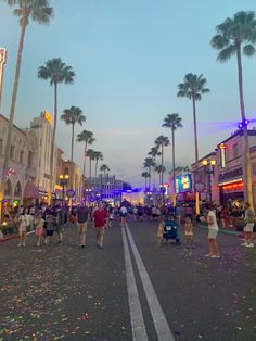 people are walking down the street in front of shops and palm trees at dusk with confetti on the ground