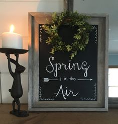 a framed sign that says spring is in the air next to a candle holder with a wreath on it