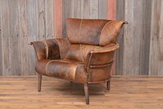 a brown leather chair sitting on top of a hard wood floor next to a wooden wall