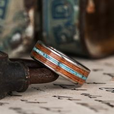 two wedding bands with wood and turquoise inlays on top of an old pipe