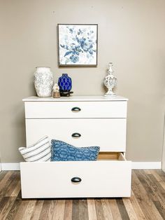 a white dresser with blue and white vases on it's top shelf next to a painting