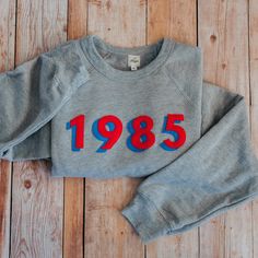 Step back in time and slip into this cozy Retro Classic Sweatshirt. Its ring-spun cotton blend and relaxed, casual fit will have you feeling comfy and looking stylish. Plus, it's got stitched lettering and a screen-printed design in classic retro colors - talk about a throwback! You'll look fly AF, like a blast from th Stitched Sweatshirt, Vintage College Sweatshirts, Year Sweatshirt, Stitch Sweatshirt, Heather Grey Sweatshirt, Retro Sweatshirts, Stylish Plus, Custom Sweatshirts, Step Back