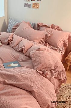 a bed with pink comforters and pillows in a room next to a chair, table and pictures on the wall