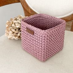 a pink basket sitting on top of a white table next to a wooden chair and flower