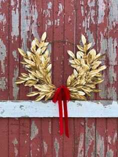 a red ribbon is tied to a gold wreath on a wooden fence with peeling paint