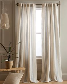 a white curtain hanging in front of a window next to a wooden table with a potted plant