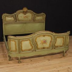 an antique green painted bed frame with flowers on the headboard and foot board, against a black background