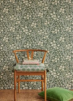 a wooden chair sitting in front of a green floral wallpaper with a pillow on the floor