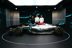 two men standing next to a silver race car