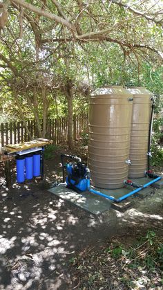 two large water tanks sitting next to each other on a dirt ground in front of trees