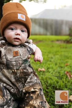 a baby is wearing a hat and sitting in the grass