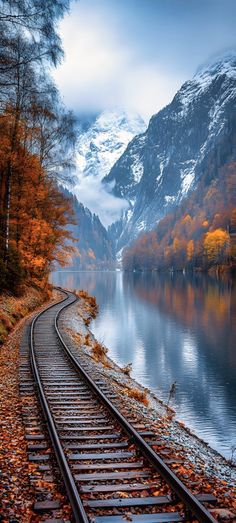 a train track running along the side of a lake with mountains in the back ground