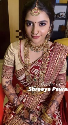 a woman in a red and gold bridal outfit with jewelry on her neck, sitting down