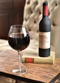 a glass of wine sitting on top of a wooden table next to a bottle of wine