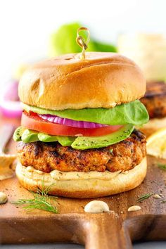 a chicken burger with lettuce, tomato and onion on a wooden cutting board