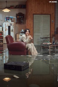 a woman sitting on a red chair in a living room next to a coffee table