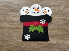 three snowmen in a black bag with red ribbon and white snowflakes on it