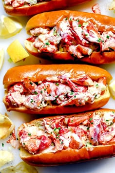 three lobster sandwiches with lemon wedges and parsley on the side, ready to be eaten