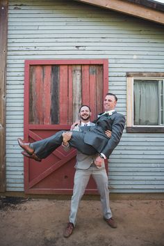 a man holding onto another man's leg in front of a building with a red door