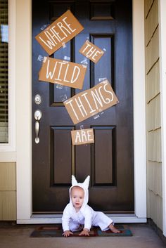 a baby is laying on the ground in front of a door with signs that say where the wild things are