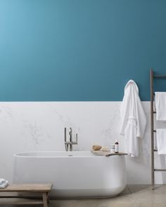 a white bath tub sitting next to a wooden ladder in a room with blue walls