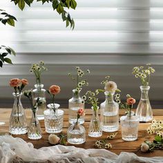 an assortment of vases with flowers in them on a wooden table next to a window