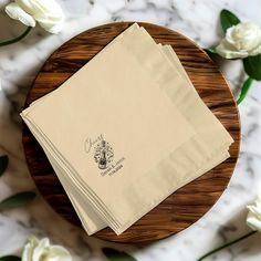 three folded napkins sitting on top of a wooden plate next to white flowers and greenery