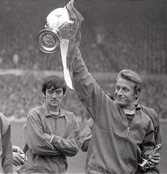 two men are holding up a trophy in front of an audience at a soccer game