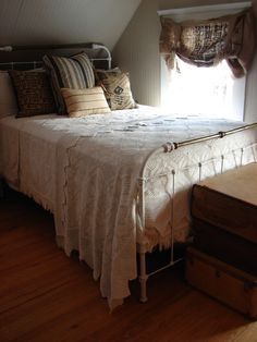 a bed sitting in a bedroom under a window next to a wooden dresser and chest