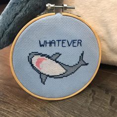 a cross stitch pattern with the words whatever on it and a shark in blue, sitting next to a stuffed animal