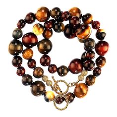 This is part of Chairish’s Fine Jewelry assortment.  Vibrant 22-Inch Multi-Colored Tiger's Eye Necklace  Add a bold and captivating touch to your jewelry collection with this 22-inch Tiger's Eye necklace. Featuring a stunning array of red, brown, gold, and blue Tiger's Eye gemstones, the design beautifully highlights the natural chatoyancy of these stones. The beads are skillfully arranged in graduated sizes of 14mm, 10mm, and 8mm for a balanced and dynamic look.  The necklace is secured with a Luxury Brown Jewelry With Natural Stones, Luxury Brown Gemstone Jewelry, Luxury Brown Jewelry With Gemstone, Brown Gemstone Beaded Necklace, Luxury Necklaces With Round Natural Stones, Luxury Necklace With Round Natural Stones, Luxury Handmade Brown Necklaces, Luxury Handmade Brown Necklace, Brown Polished Beads Round Necklace