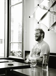 a black and white photo of a man sitting at a table with wine glasses in front of him