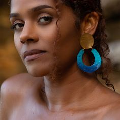 a close up of a person wearing large blue and gold earring with shells on it